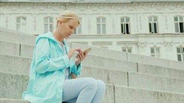 Bir kadın turist bir akıllı telefon kullanır. Kopenhag'da güzel bir binanın zemin karşı adımlar üzerinde oturur