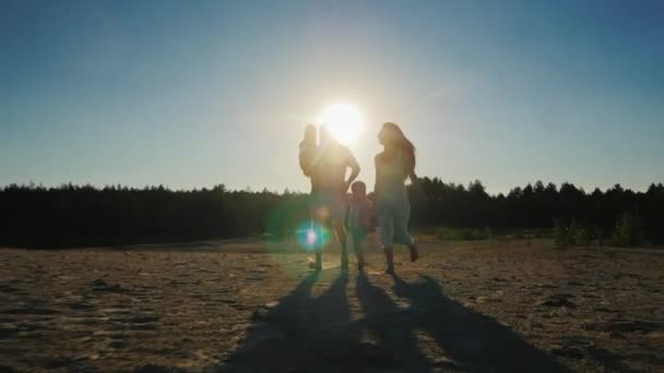 Щаслива сім'я, батьки і двоє синів, бігають через пісок на заході сонця. Начерки стрільби — стокове відео