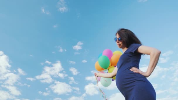 Happy těhotná žena hrající s balónky proti modré obloze — Stock video