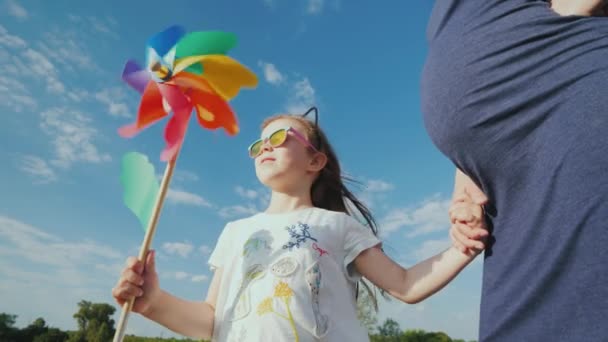 Веселая девушка играет на игрушечной ветряной мельнице рядом со своей беременной матерью — стоковое видео