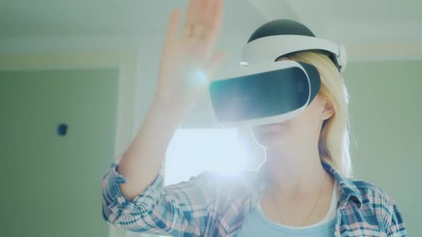 A woman in a virtual reality helmet looks at a room in her new home. The sun with a flare shines from behind the window. Dream house designing — Stock Video