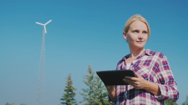 A young woman uses a tablet, in the background running a home wind power station. Green energy — Stock Video