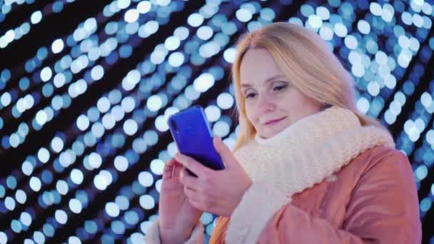 Çekici bir kadın Festival çelenk şehrin arka plan üzerinde bir akıllı telefon kullanır — Stok video