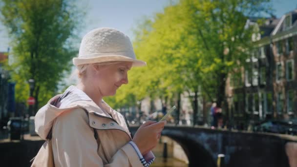 Jonge vrouw met een smartphone tegen de achtergrond van het uitzicht op de pittoreske stad in Amsterdam — Stockvideo