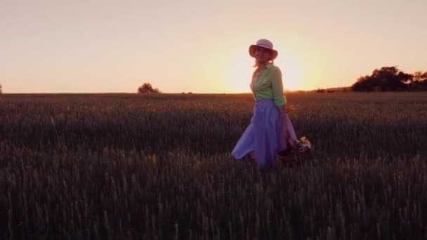 En lycklig sorglös kvinna med en korg med blommor promenader i solnedgången i en pittoresk plats — Stockvideo