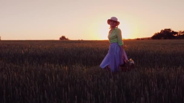 野生の花のバスケットと幸せな屈託のない女は美しい場所で夕暮れ歩く — ストック動画