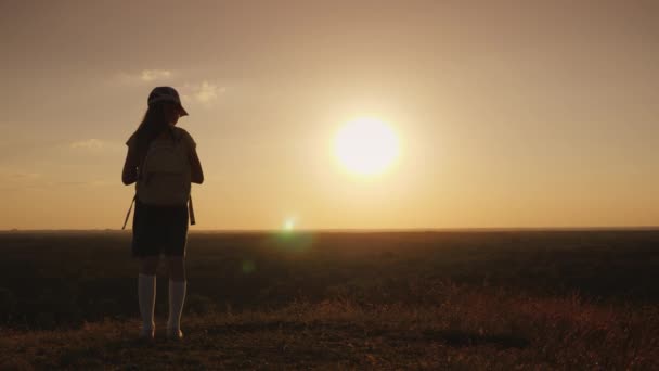 Uma criança com uma mochila atrás dos ombros admira o pôr-do-sol na colina. Crianças Sonho de Viagem — Vídeo de Stock