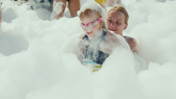 Vacaciones divertidas para niños con toda la familia, una joven mujer activa con su hija pequeña se divierten retozando en una fiesta de espuma en la playa — Vídeos de Stock