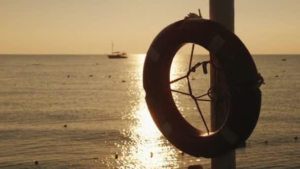Hajnal a tengeren, az előtérben egy életgyűrű lóg, a távolban a hajó látható. Szcenikus táj kora reggel — Stock videók