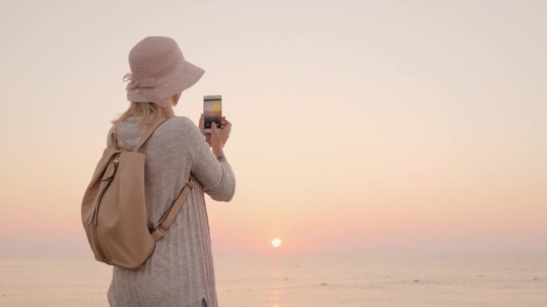 Een nieuwe dag, nieuwe kansen en vervulling van verlangens, het meisje in de hoed corrigeert het moment van de zonsopgang op de telefoon — Stockvideo