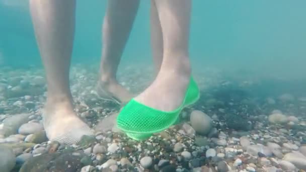 Protezione dei piedi durante il nuoto in mare. Gambe in scarpe protettive sul fondo di ghiaia del mare. Bagno sicuro nel concetto di mare — Video Stock