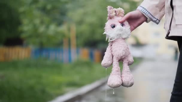 Eine Frau hält ein durchnässtes Spielzeug in der Hand. Wasser tropft davon, es regnet — Stockvideo