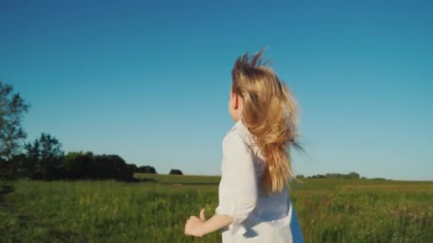 Una chica con el pelo largo corre con un avión de papel en la mano. Concepto de sueños de bebé. Vista trasera — Vídeos de Stock