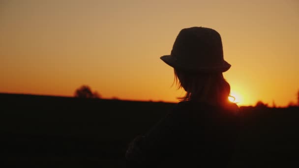 Een jonge vrouw in een hoed bewondert de zonsondergang in een schilderachtige plaats — Stockvideo