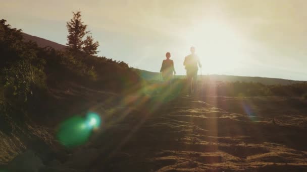 El amanecer del sol en las montañas. Las siluetas de dos viajeros se encuentran, descienden a lo largo de un camino de montaña — Vídeos de Stock