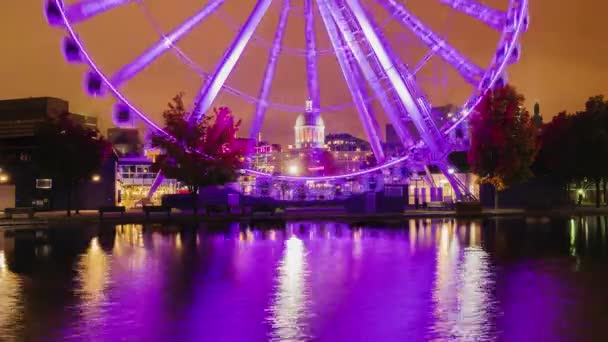 Uma roda gigante brilhantemente iluminada com luz de fundo rosa na antiga área portuária de Montreal, Canadá. Lindamente refletido na água — Vídeo de Stock