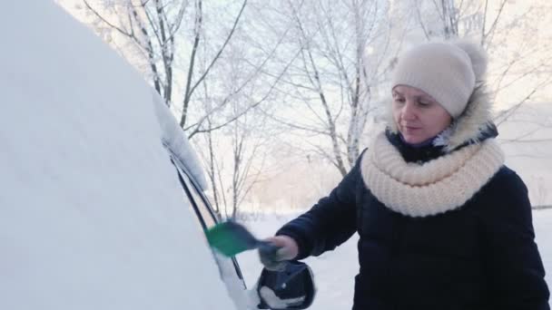 Женщина убирает снег со своей машины в зимний день — стоковое видео