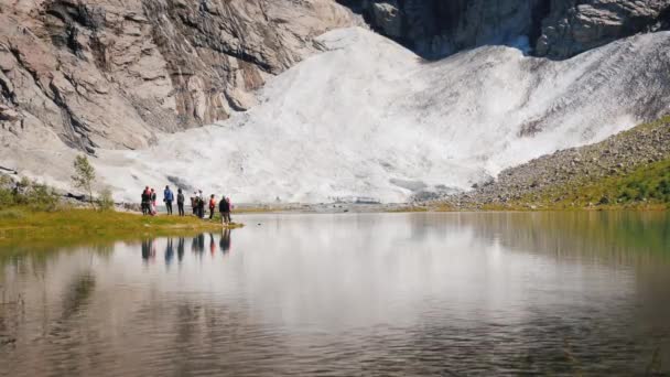 小さな湖とノルウェーの氷河の近くの観光客のグループ。北欧の自然と観光 — ストック動画