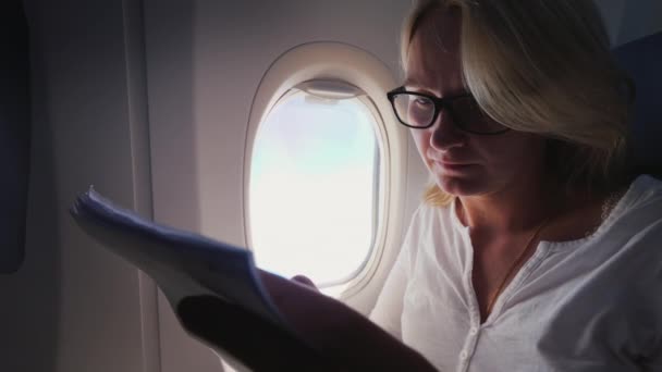 Una mujer de mediana edad mira documentos en papel en vuelo . — Vídeo de stock