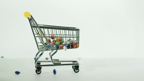 In a small shopping trolley pour round candy in multi-colored glaze. Buying sweets — Stock Video