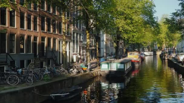 アムステルダムの運河の日没の前に、の時間。都市の古い部分の風光明媚なビューは、ボート付近の管壁と自転車 — ストック動画