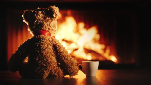 A bear cub with a cup of tea sits opposite the fireplace. Comfort and warmth in the house — Stock Photo, Image