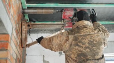 İşçi güçlü bir elektrikli aletle duvarı deliyor. İletişim kurmak için delikler açar