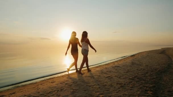 Ung mor med sin dotter, en tonåring som promenerar på stranden vid solnedgången. — Stockvideo