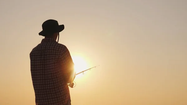 Молодой человек в шляпе рыбалка на пляже на закате — стоковое фото