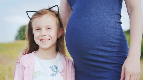 Uma menina doce com orelhas de gatos fica perto da barriga de sua mãe grávida — Vídeo de Stock