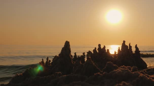 El sol poniente brilla en el castillo de arena en la orilla del mar — Vídeos de Stock