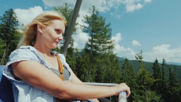 Een actieve vrouw geniet van een ritje op een kabelbaan over een bos omgeven door bergen — Stockvideo