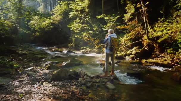 Uma mulher fotógrafa tira fotos de uma bela paisagem em uma floresta pitoresca no início da manhã — Vídeo de Stock