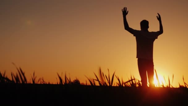 Un adolescent admire le coucher du soleil. Debout sur le terrain, il met ses mains derrière le cou, la vue arrière — Video