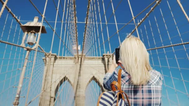 Vista trasera: Una mujer es fotografiada con el telón de fondo del Puente de Brooklyn, uno de los lugares más populares y reconocibles de Nueva York — Vídeo de stock