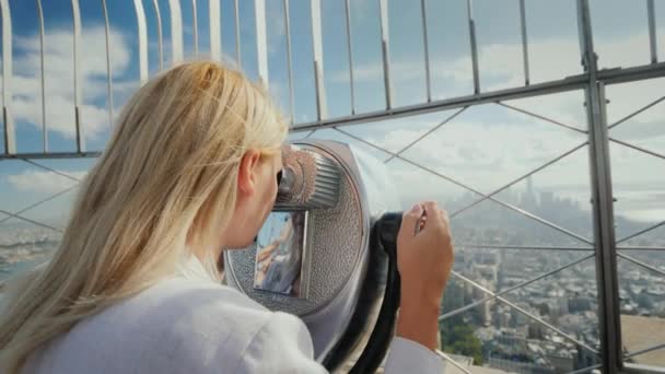 Una mujer admira una hermosa vista de la ciudad de Nueva York, mira a través de un telescopio — Vídeos de Stock