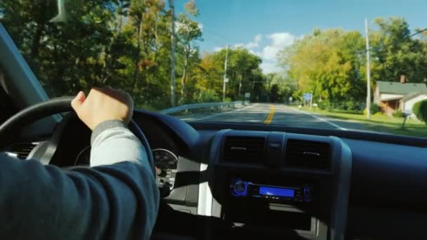 Egy férfi keze egy autó kormányán, egy tipikus amerikai külvárosban. — Stock videók