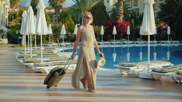 Una donna con una borsa da viaggio viene sistemata nell'hotel-resort per una vacanza, passando vicino alla piscina. Vista laterale — Video Stock