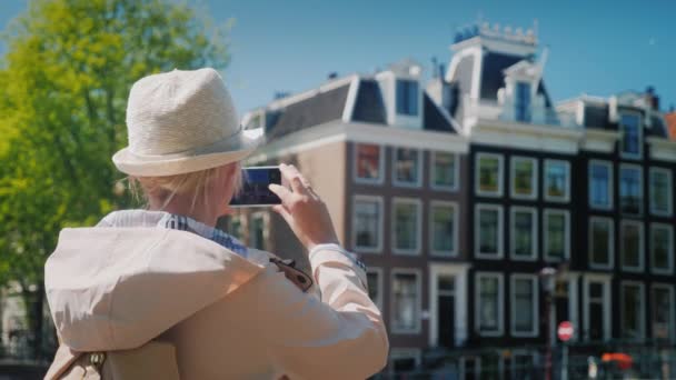 Eine frau mittleren alters fotografiert schöne gebäude und einen kanal in amsterdam. travel europe concept — Stockvideo