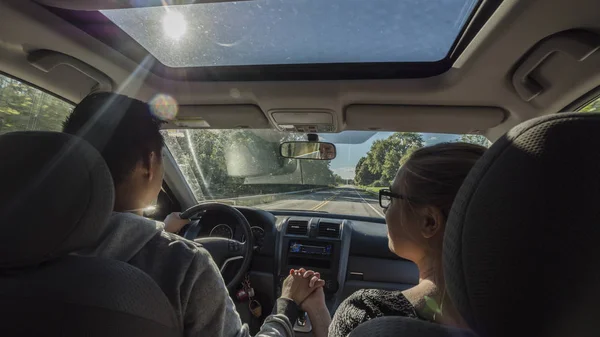 Pareja multiétnica montando en un coche, un hombre sosteniendo una mano de mujer — Foto de Stock