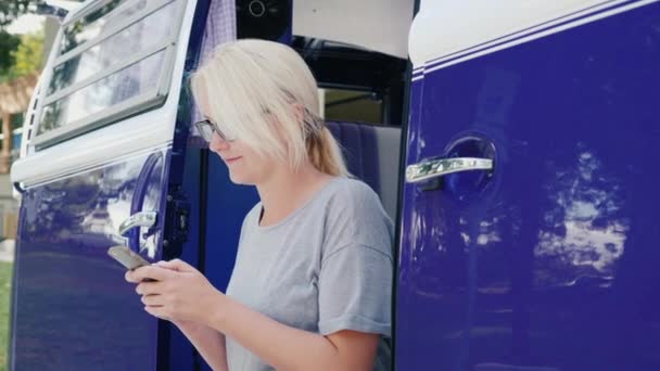 Eine Frau benutzt ein Smartphone. sitzt auf der Stufe des violetten Retro-Van — Stockvideo