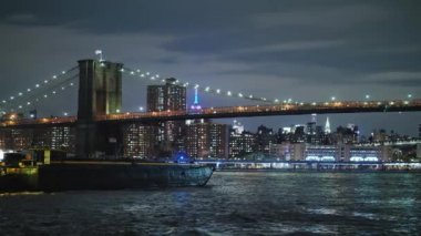 Manhattan'ın gece ışık arka plan üzerinde New York'ta Brooklyn Köprüsü altında kargo mavna yelken