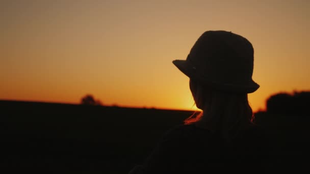 Silhueta de uma jovem mulher admirando o pôr do sol, olhando para a frente — Vídeo de Stock