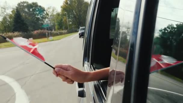 Mano con una pequeña bandera canadiense. ondeando una bandera desde la ventana del coche — Vídeos de Stock