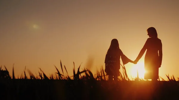 A mãe e a filha estão a admirar o pôr do sol, de mãos dadas. Conceito de infância feliz — Fotografia de Stock