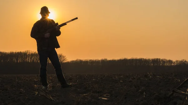 Un hombre con un arma en un campo al atardecer. Apertura de la temporada de caza — Foto de Stock