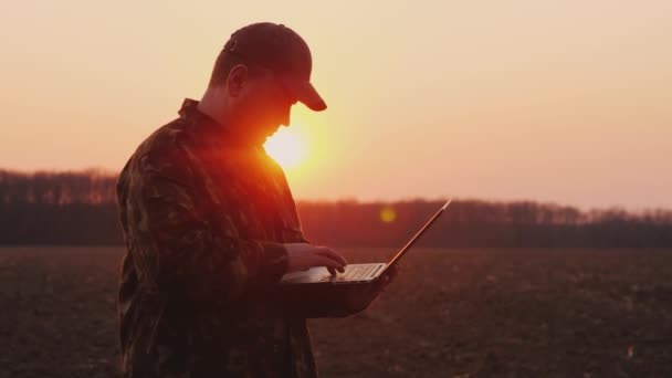 Un agricultor de mediana edad usa una computadora portátil en un campo al atardecer. Planes de siembra — Vídeos de Stock