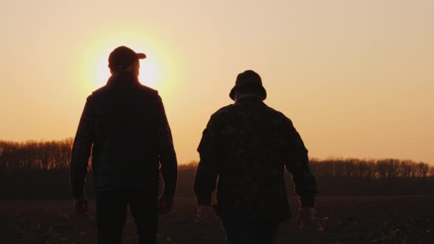 Les agriculteurs père et fils marchent à travers le champ au coucher du soleil, bavardant — Video