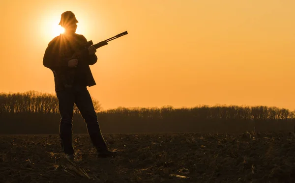 Silueta de cazador con pistola. De pie en un campo al atardecer en pleno crecimiento — Foto de Stock