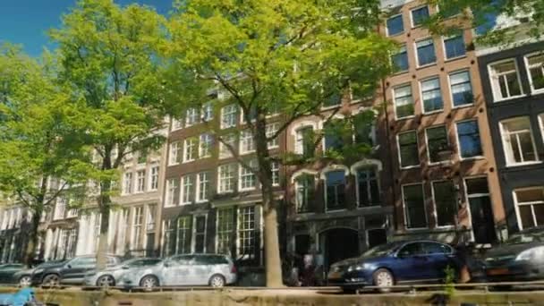 Navegue ao longo do canal em Amsterdã. Uma vista das casas bonitas velhas, uma fileira de carros estacionados, o sol é refletido lindamente nas janelas. Turismo nos Países Baixos — Vídeo de Stock